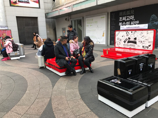 신세계디에프가 서울 명동예술극장 앞 광장에 아트힐링공간 '예술신(新)세계'를 운영한다. 관광객들이 이곳에 설치된 캐리어 형태의 벤치에 앉아 휴식을 취하고 있다. <신세계디에프 제공>
